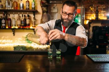 Barkeeper pouring alcoholic beverage in glass behind restaurant bar counter