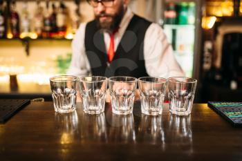 Empty glasses on wooden bar counter, bartender working on background