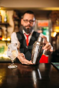 Barman with shaker behind a bar counter with glass of alcohol beverage
