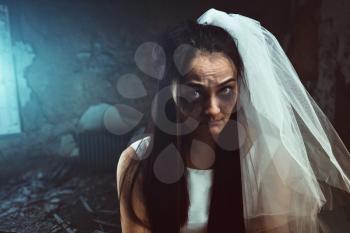 Disheveled bride with tear stained face in white veil, abandoned house interior on background