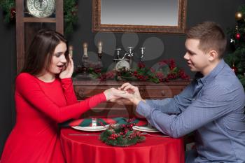 Happy man puts a wedding ring on womans hand. Rich interior of luxury restaurant on background