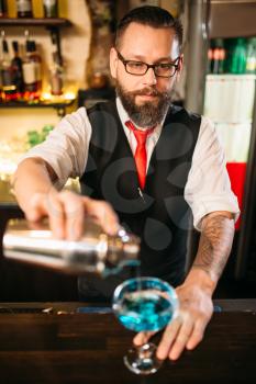 Barman with shaker making alcohol cocktail behind a bar counter