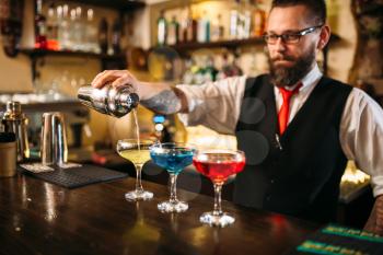 Barman with shaker making alcohol cocktails behind a bar counter in nightclub