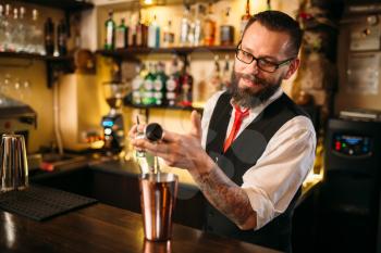 Bartender pouring alcohol beverage in metal glass at restaurant