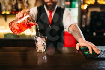 Barman pouring alcoholic drink in glass. Bartender flairing in restaurant