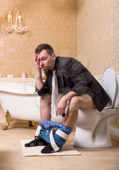 Drunk man with pants down sitting on the toilet bowl. Bathroom interior in retro style on background