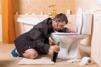 Funny drunk man with bottle of wine sick in the toilet bowl. Luxury bathroom interior on background