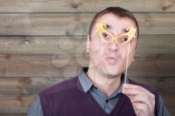 Young man with funny glasses on a stick, wooden background. Fun photo props and accessories for shoots