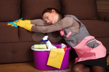 Tired female cleaning servisce worker in uniform and rubber gloves asleep on a couch. Housekeeping concept