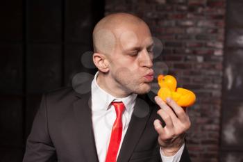 Special agent kissing little toy duck. Contract killer in suit and red tie shows his fears and secrets. Hired murderer wallpaper or background concept