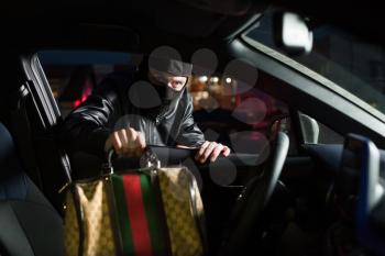 Male thief with balaclava on his head steals bag from car on parking. Carjacking danger concept. Carjacker unlock vehicle. Auto transport crime