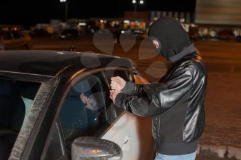Male carjacker with balaclava on his head trying to open car door with ruler. Thief unlock vehicle. Auto transport insurance marketing