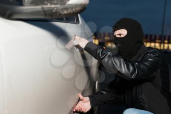 Male thief with balaclava on his head trying to open car door. Carjacker unlock vehicle