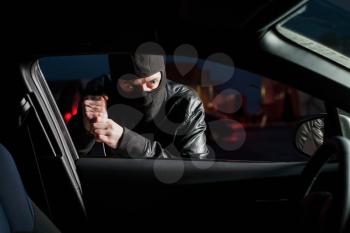 Male carjacker with balaclava on his head trying to open car door with screwdriver. Thief unlock vehicle. Auto transport crime