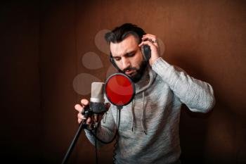Male singer recording a song in music studio. Vocalist in headphones against microphone. Audio recording. Professional digital sound technologies
