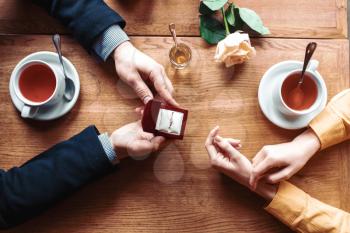 Female and male hands with wedding ring top view, wooden table, rose and cups on background. Couple romantic date. Marriage proposal