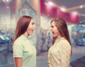Two girls screams at each other in shopping center. Women quarrel