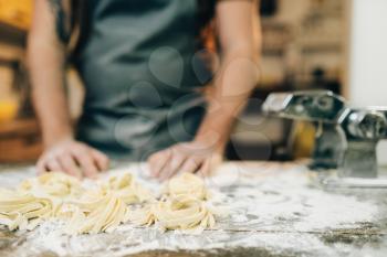 Male chef against wooden kitchen table with homemade pasta. Fettuccine preparation process