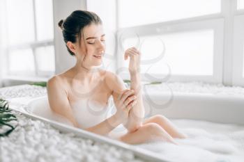 Sexy young woman rubs the body with foam in the bath. Luxury bathroom with palm branch decor, comfortable resting
