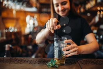 Female barman mixing at the bar counter in pub. Woman bartender prepares beverage. Barkeeper occupation