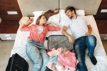 Couple lies on the bed with opened suitcase, top view. Fees on journey concept. Luggage preparation