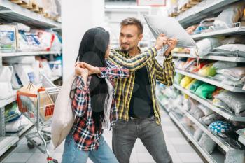 Playful couple in supermarket, pillow fight. Male and female customers on family shopping. Man and woman purchasing goods for the house