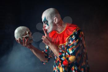 Portrait of mad bloody clown shows the quiet sign to the skull, face in blood. Man with makeup in halloween costume, maniac