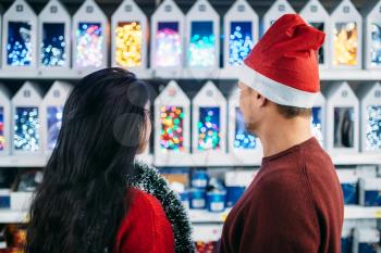 Young couple looks on christmas gifts in supermarket, family tradition. December shopping, choosing of holiday decorations