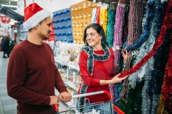 Young couple choosing holiday fluffy garland, purchase of christmas decoration in supermarket, family tradition. December shopping