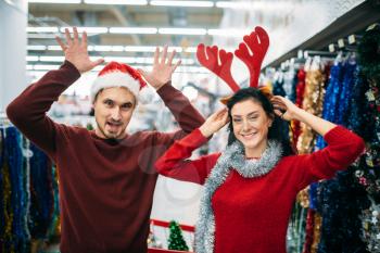 Playful couple choosing christmas decorations in supermarket, family tradition. December shopping of holiday goods