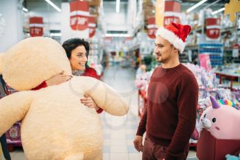 Young couple choosing plush toys on christmas in supermarket, family tradition. December shopping of new year holiday goods and decorations