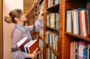 Young woman takes book from shelf in university library. Female person in knowledge depository