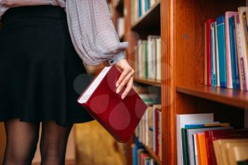 Female person with book at the bookshelf in university library. Woman in knowledge depository, education