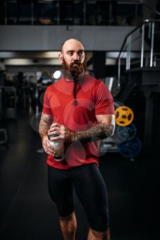 Strong athlete drinks water after exercise with dumbbells, workout in gym. Bearded sportsman on training in sport club, healthy lifestyle