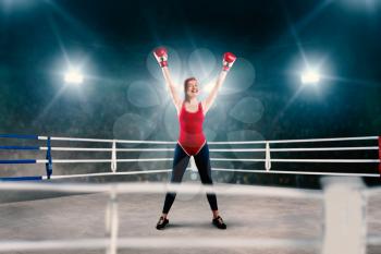 Female boxer in red bandages and sportswear hands up on the ring, side view. Winner woman on boxing ring