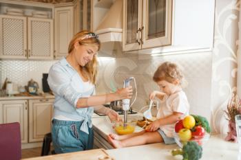 Young mother and her daughter whisk the ingredients for cake with a blender in a bowl. Cute woman and little kid cooking on the kitchen, pastry preparation. Happy family prepares sweets