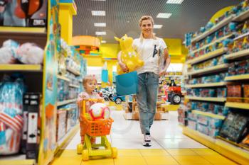 Mother with her little girl buying a lot of toys in kids store. Mom and child in supermarket together, family shopping, happy buyers
