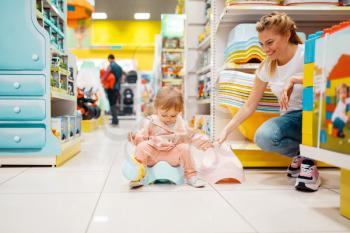 Mother with her little girl choosing baby potty in kids store. Mom and child in supermarket together, family shopping