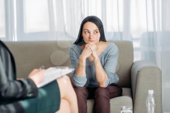 Female patient sitting on sofa at psychotherapist reception. Female doctor writes notes in notepad, professional psychology support