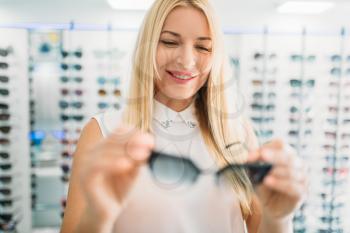 Female optician shows sunglasses in optics store. Selection of eyes protection with professional optometrist, optometry concept