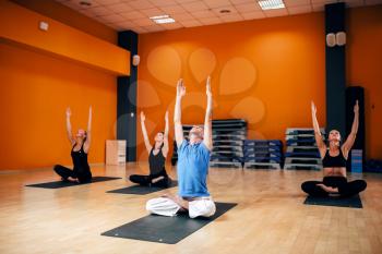 Relaxation, female group with trainer sitting in yoga pose, workout in gym. Yogi indoor