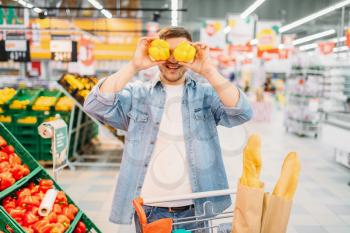 Male person funs with yellow peppers in a supermarket, family shopping. Customer in shop, buyer in market