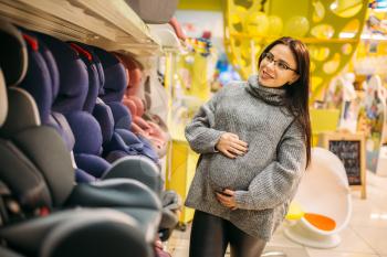 Pregnant woman choosing child car seat in store. Goods for safe transportation of children