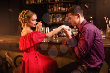 Romantic date in restaurant, attractive woman in red dress flirts with man against bar counter. Love relationship, night lifestyle