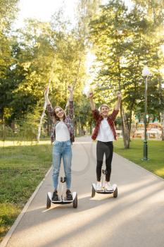 Young happy couple riding on gyro board in summer park. Outdoor recreation with electric gyroboard. Eco transport with balance technology, electrical gyroscope vehicle