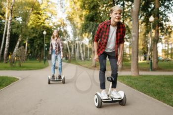 Young couple riding on gyro boards in summer park. Outdoor recreation with electric gyroboard. Eco transport with balance technology, electrical gyroscope vehicle