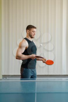 Man with two rackets stuffs blows in ping pong indoors. Male person in sportswear at the table with net, training in table-tennis club