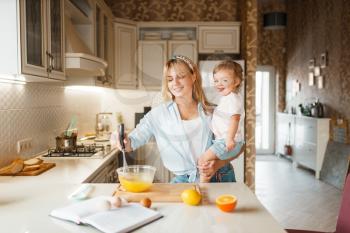 Young mother and her daughter mixing fruits in a bowl. Cute woman and little girl cooking on the kitchen, cake preparation. Happy family prepares sweet dessert, ingredients on the table