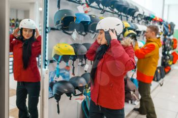 Young woman trying on helmet for ski or snowboarding at the mirror, side view, sports shop. Winter season extreme lifestyle, active leisure store, buyers choosing protect equipment