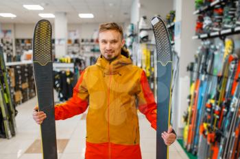 Man at the showcase holding downhill ski in his hands, front view, shopping in sports shop. Winter season extreme lifestyle, active leisure store, buyer choosing skiing equipment